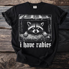 Black t-shirt with a stark white graphic of a raccoon peeking from a drainpipe, text reads "i have rabies".