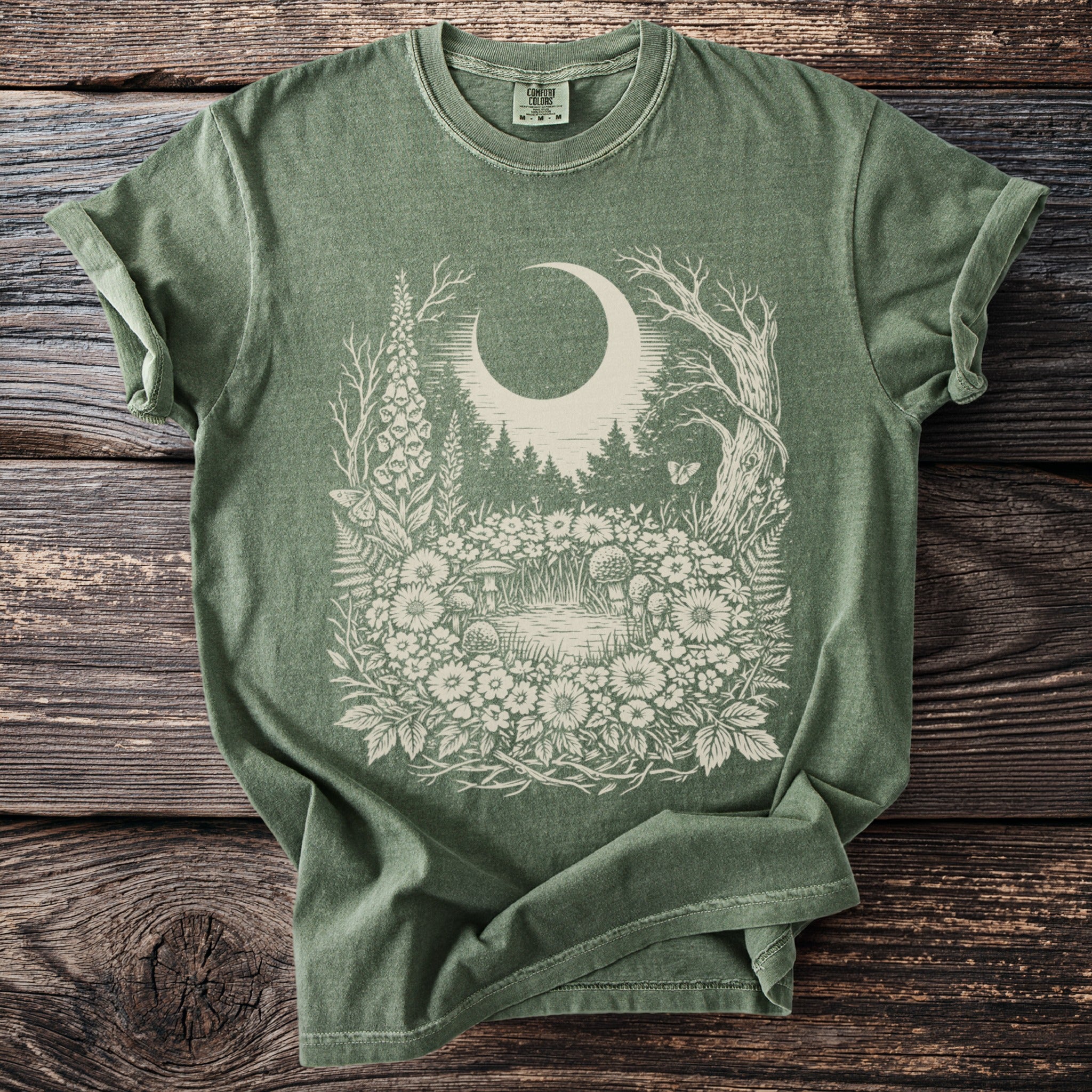 Green t-shirt with a cream moon, forest, and floral design.