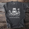 Dark gray t-shirt with a detailed graphic of a toad and mushrooms, text reads "currently decomposing".