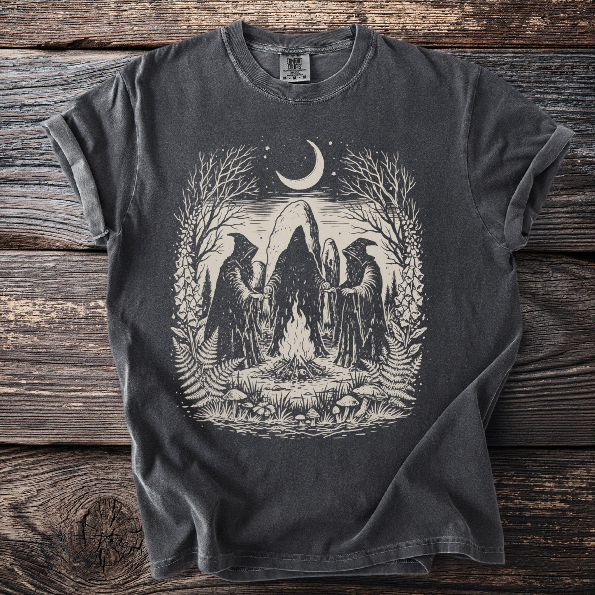 Dark t-shirt with occult scene: hooded figures, bonfire, moon, and nature elements.