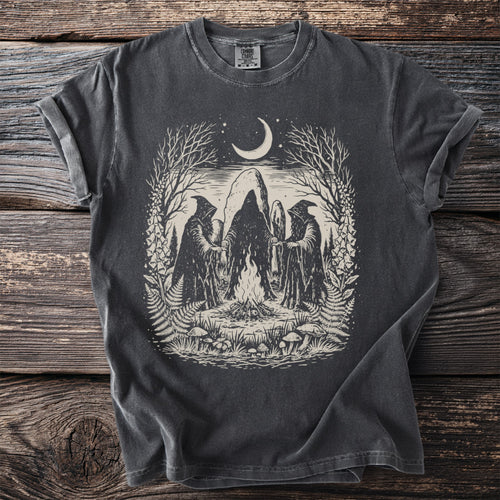 Dark t-shirt with occult scene: hooded figures, bonfire, moon, and nature elements.