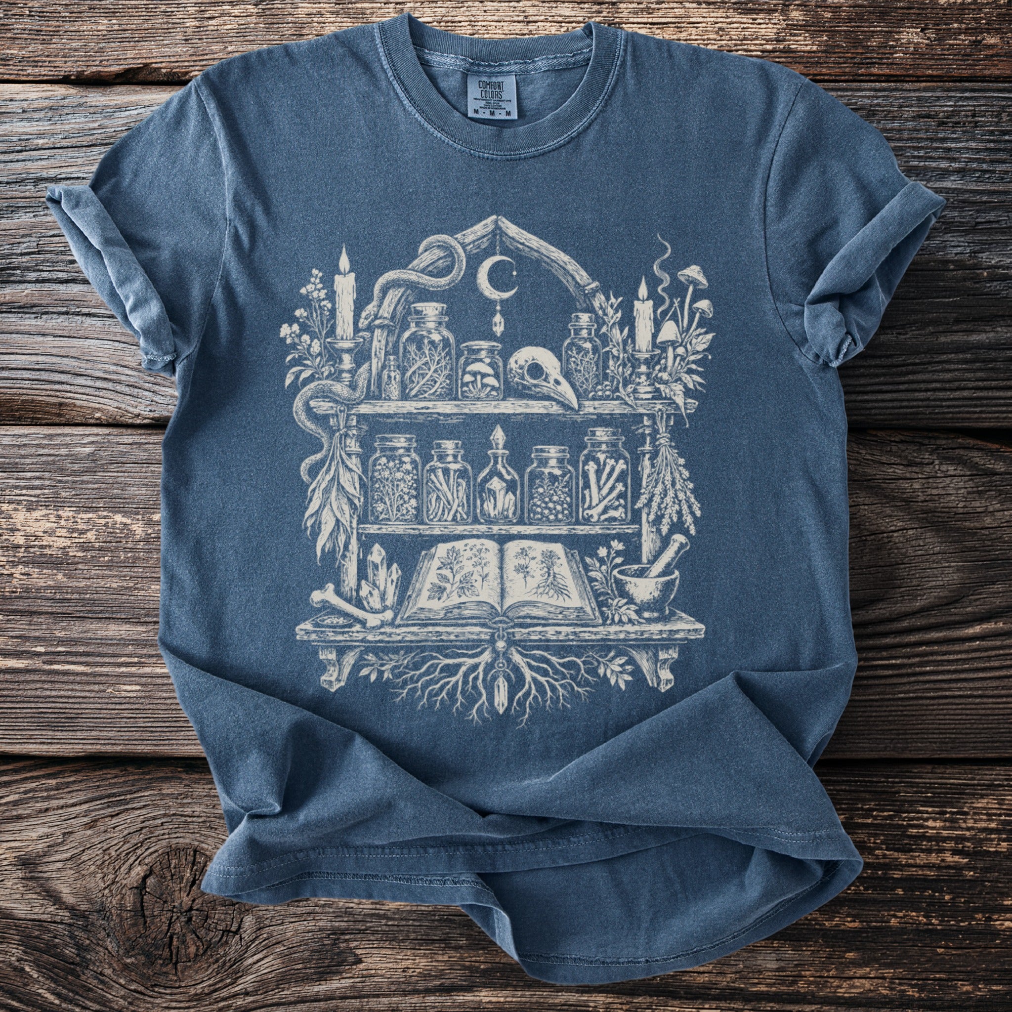 Blue Comfort Colors t-shirt with a white occult shelf graphic featuring a skull and jars.