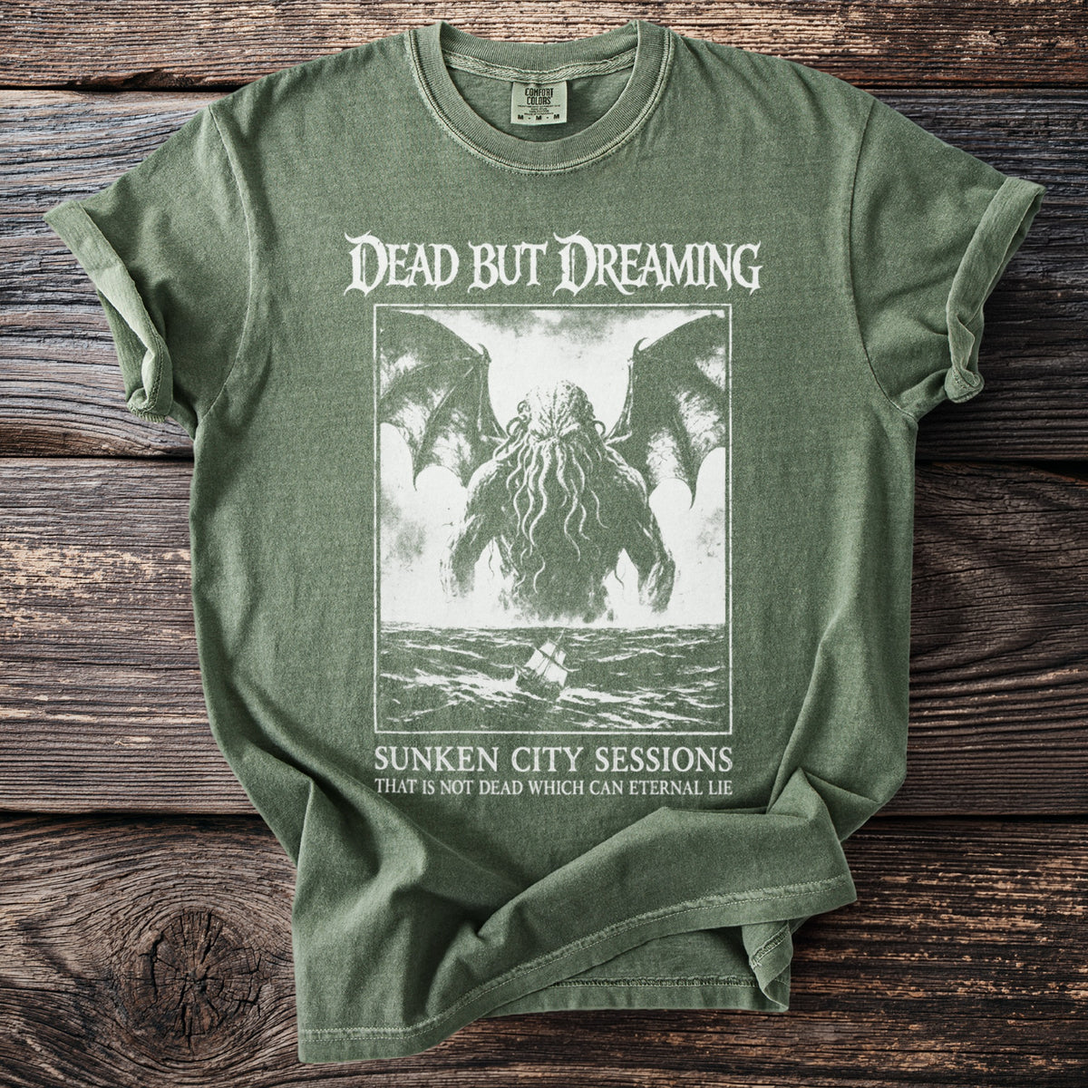 Olive green t-shirt with "Dead But Dreaming" and tentacled creature graphic, "Sunken City Sessions" text.