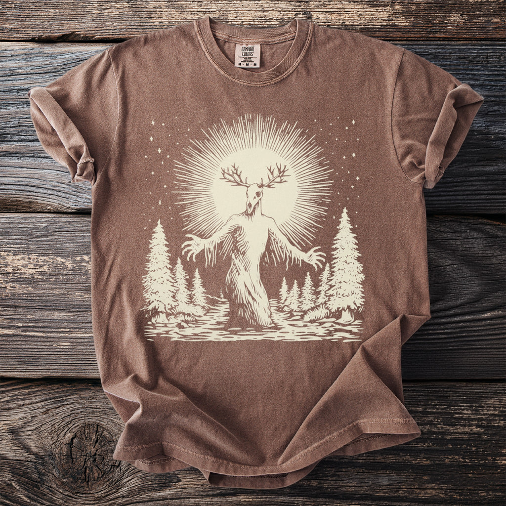 Brown comfort colors t-shirt with a pale tan graphic of a deer-headed cryptid in a forest.
