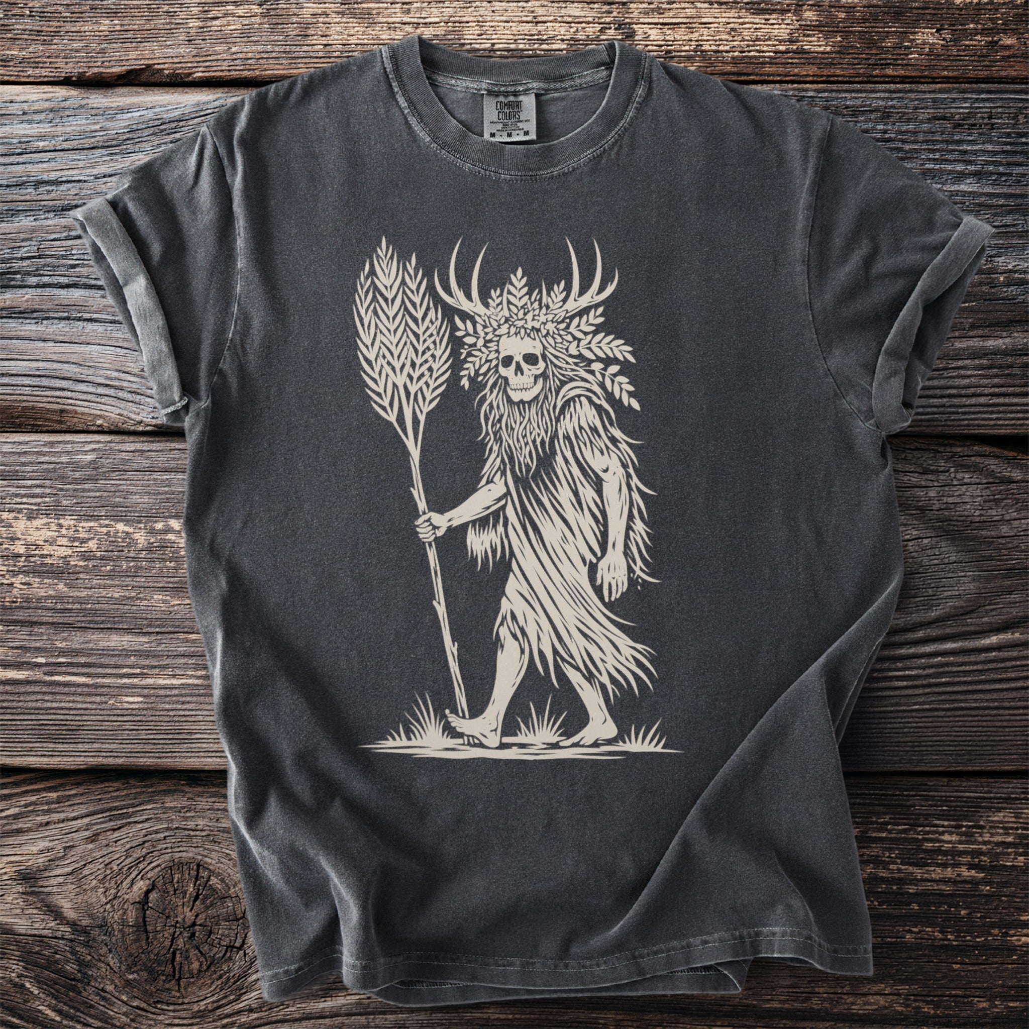 Skull figure with antlers and plant motifs holding a stalk on a dark t-shirt.