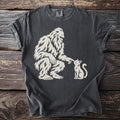 Bigfoot playfully touches a cat's nose on this dark grey t-shirt.