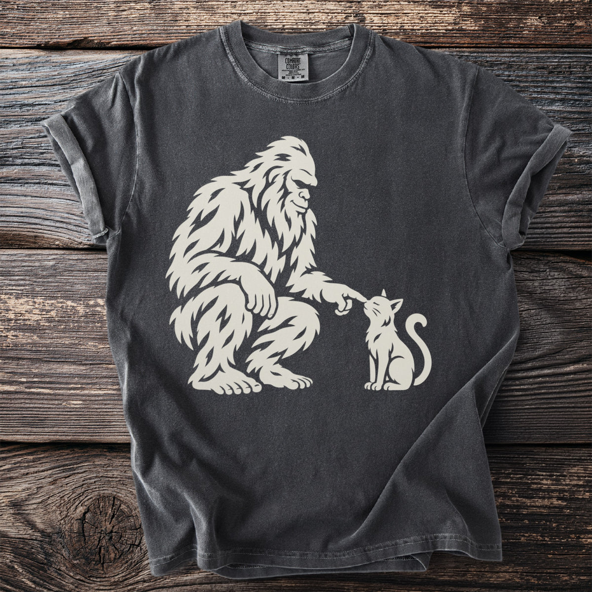 Bigfoot playfully touches a cat's nose on this dark grey t-shirt.
