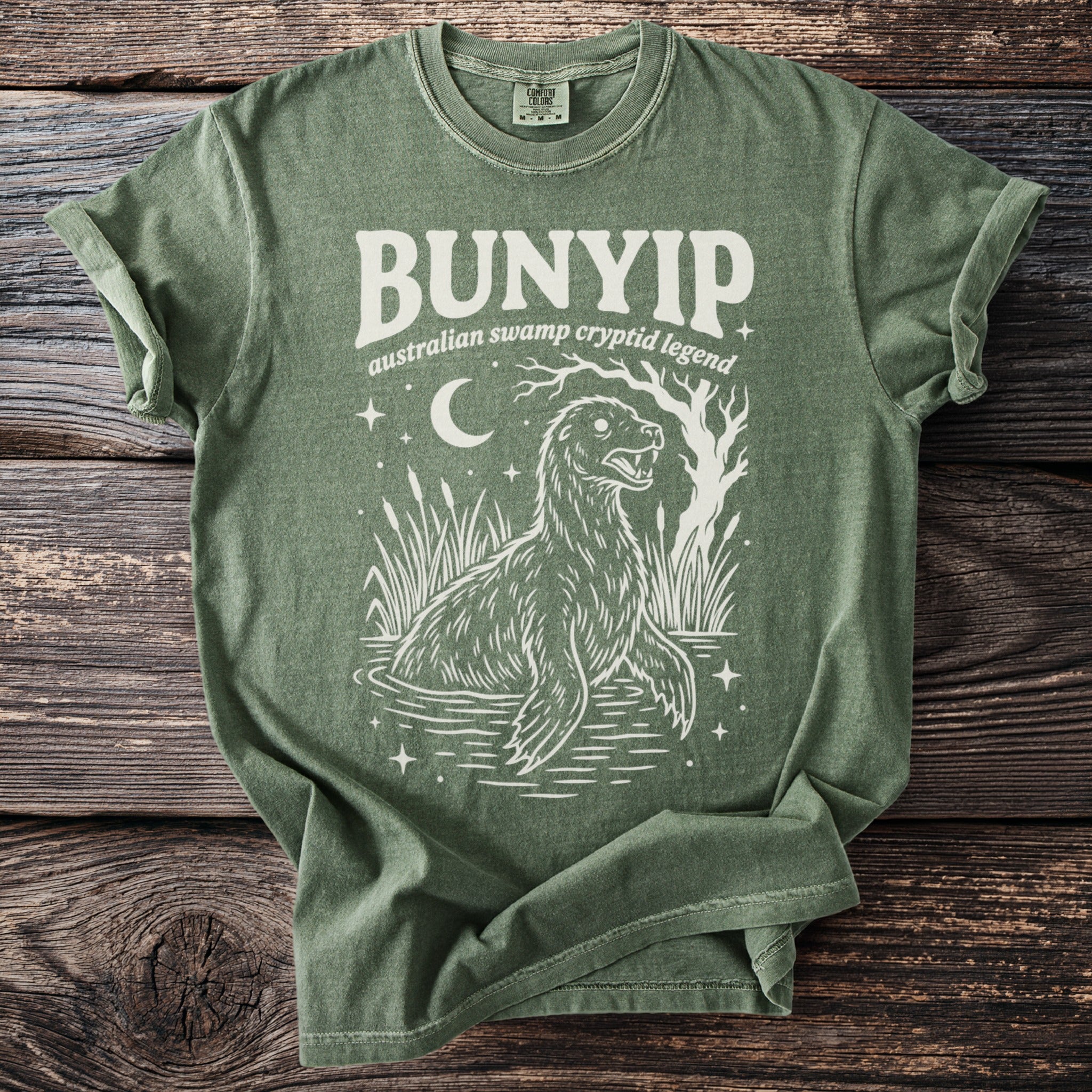 Green t-shirt with "Bunyip Australian swamp cryptid legend" text and illustration.
