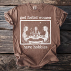 Brown t-shirt with graphic of three women around a table with text "god forbid women have hobbies".