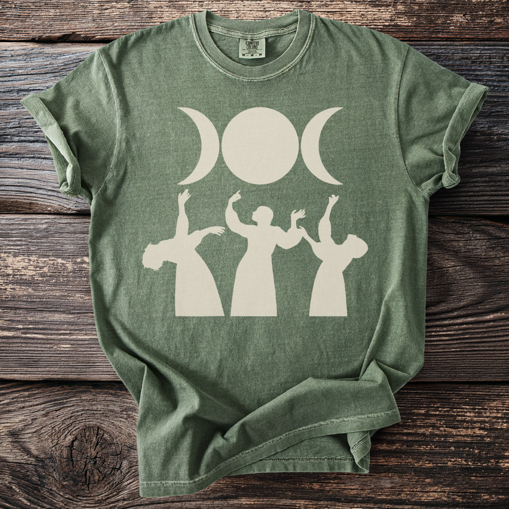 Green t-shirt with cream triple moon and dancing figures graphic.
