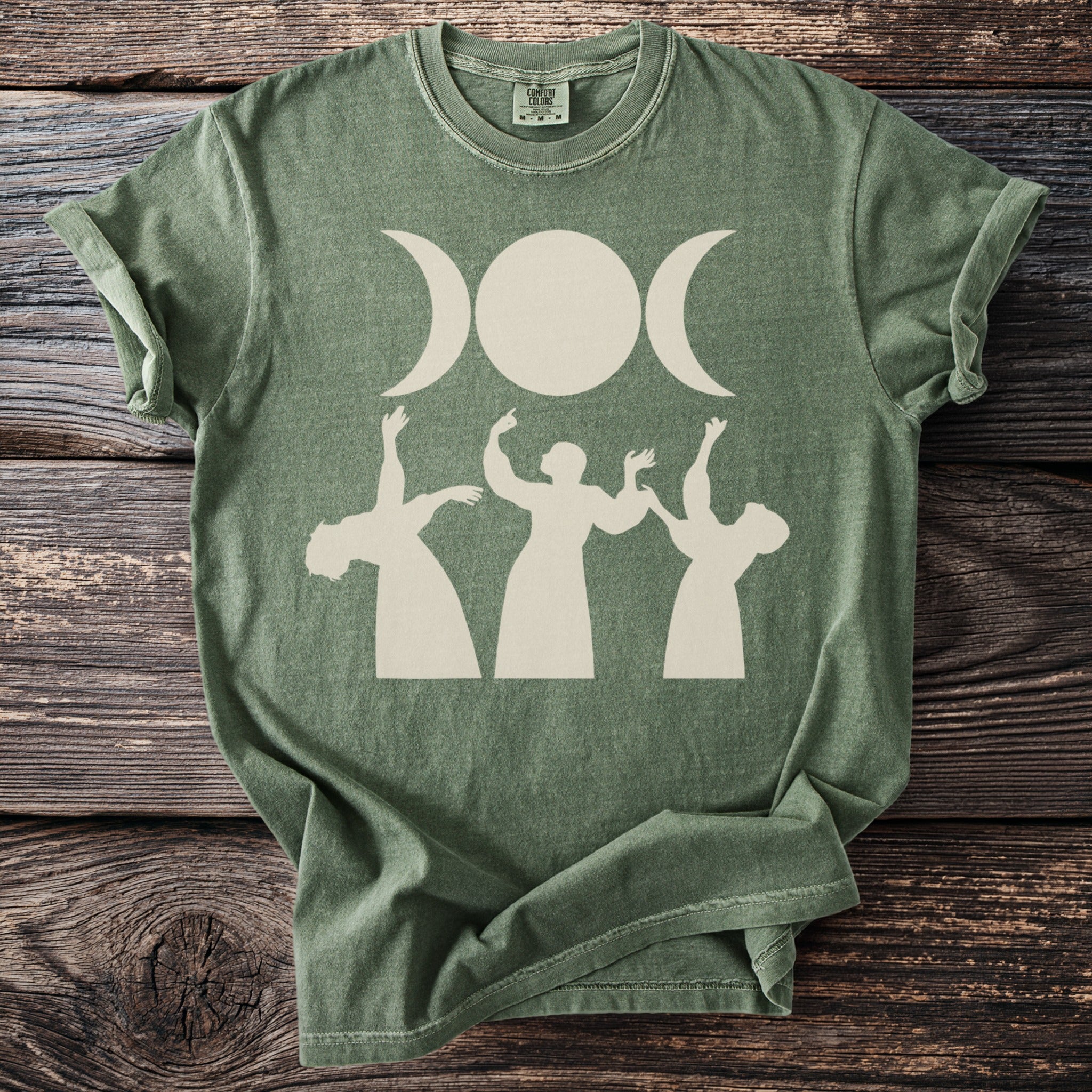 Green t-shirt with cream triple moon and dancing figures graphic.