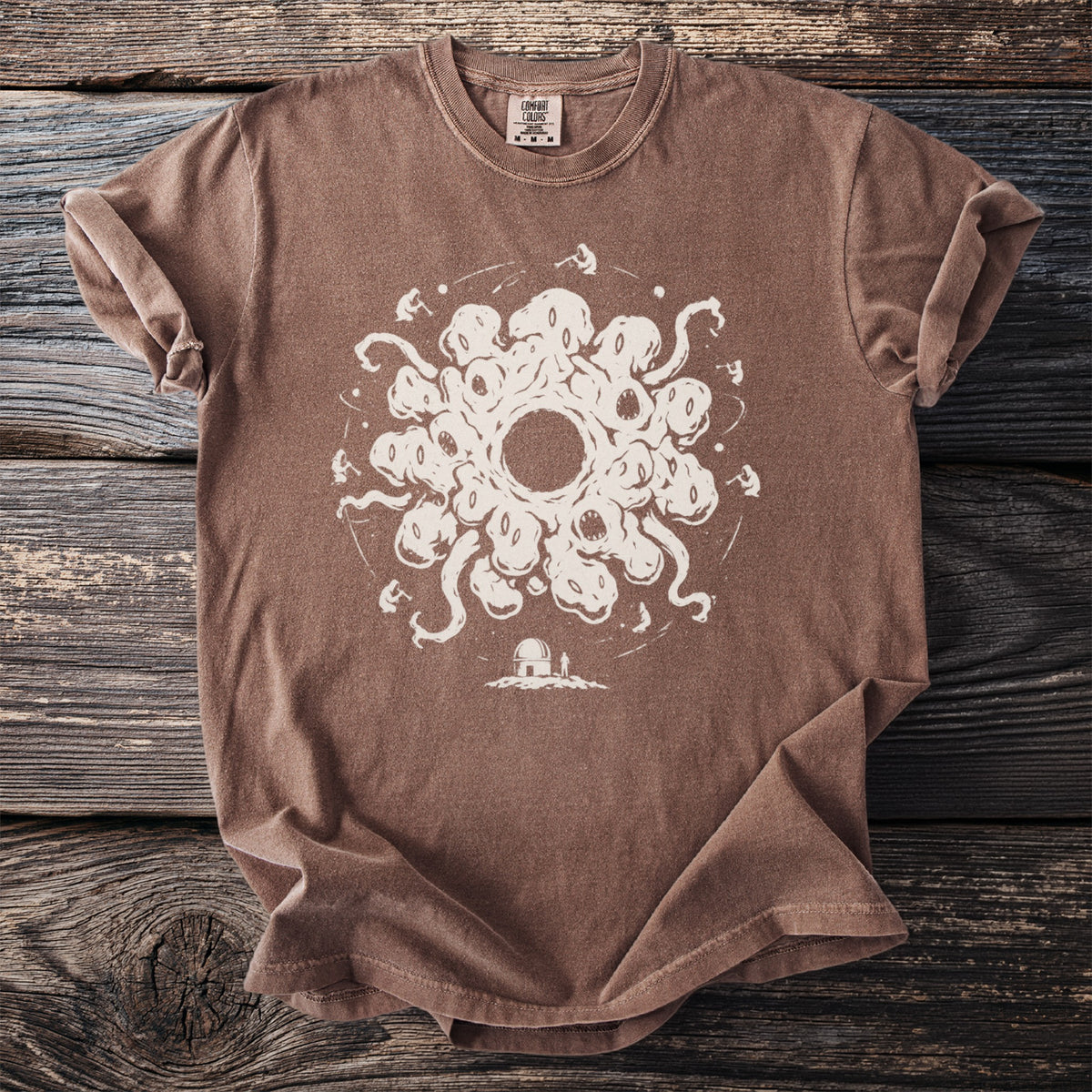 Brown t-shirt with a cream-colored graphic of a cosmic entity and an observatory.