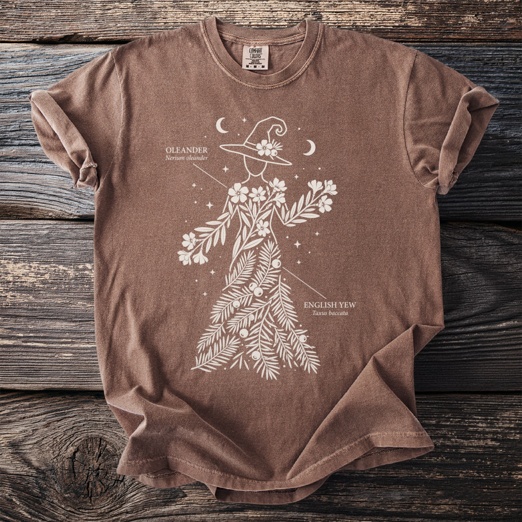 Brown t-shirt with white line art of a witch adorned with oleander and English yew.