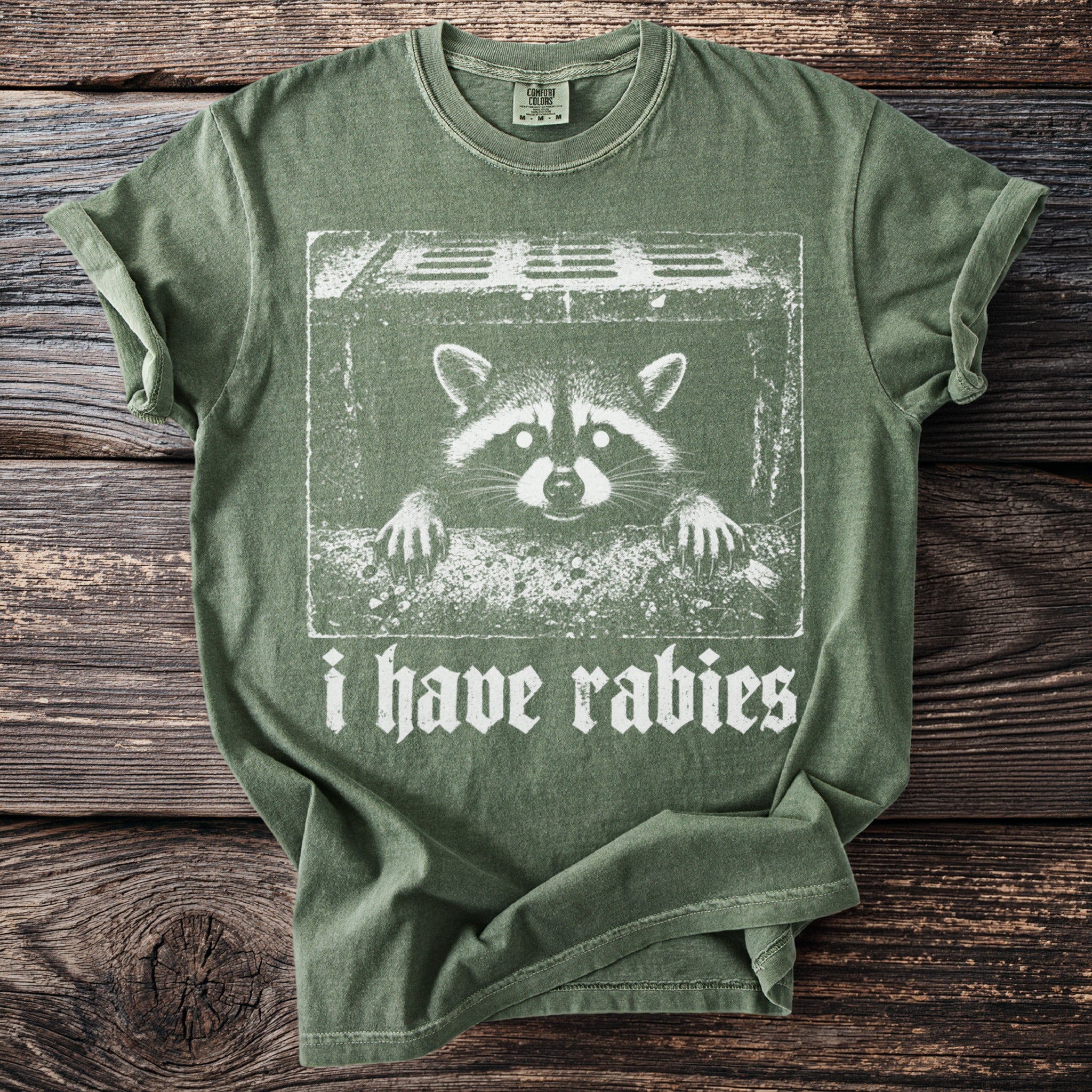 Green t-shirt with a distressed print of a raccoon and the text "i have rabies".