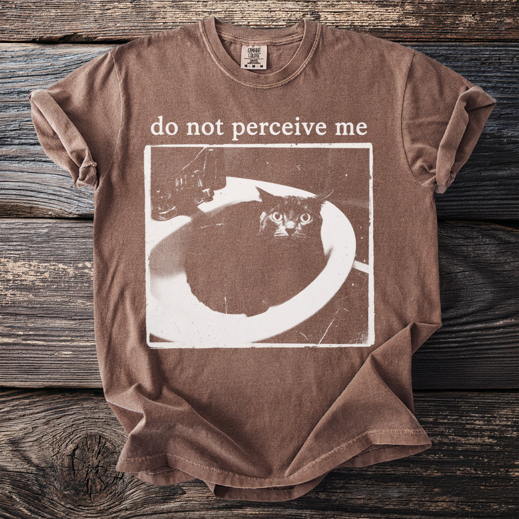 Brown t-shirt with a distressed print of a scared cat in a sink and text "do not perceive me".