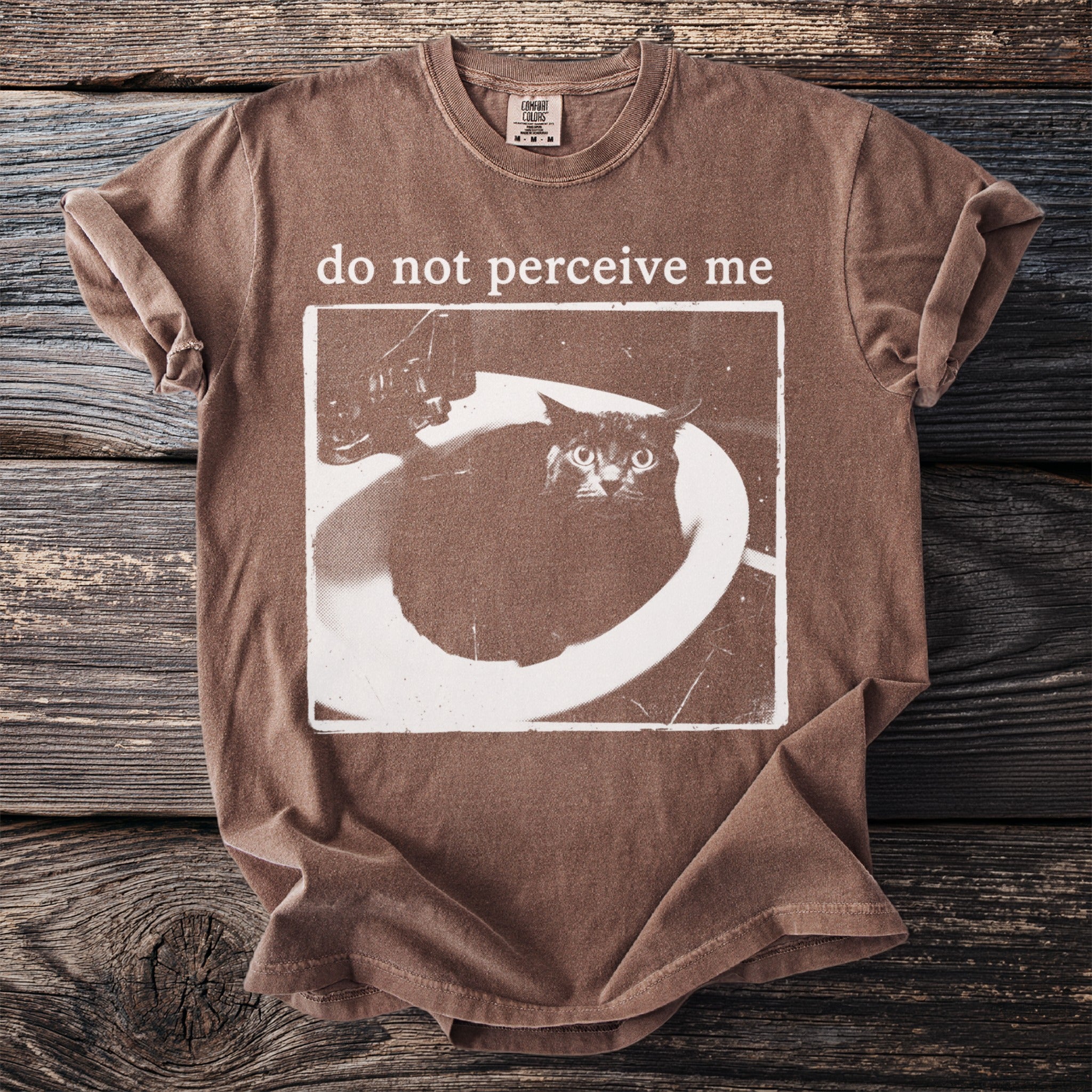 Brown t-shirt with a distressed print of a scared cat in a sink and text "do not perceive me".