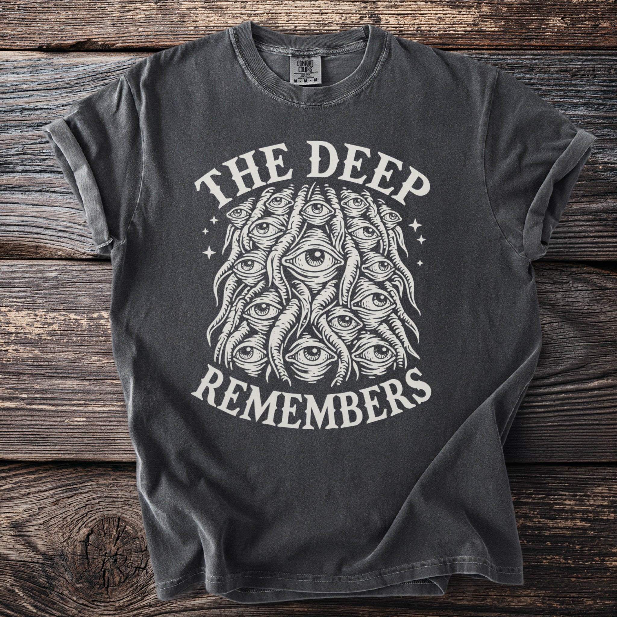 Dark grey t-shirt with "The Deep Remembers" and a cluster of eyes graphic.