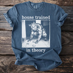 Blue t-shirt with a graphic of a werewolf cleaning paw prints and the text "house trained in theory."