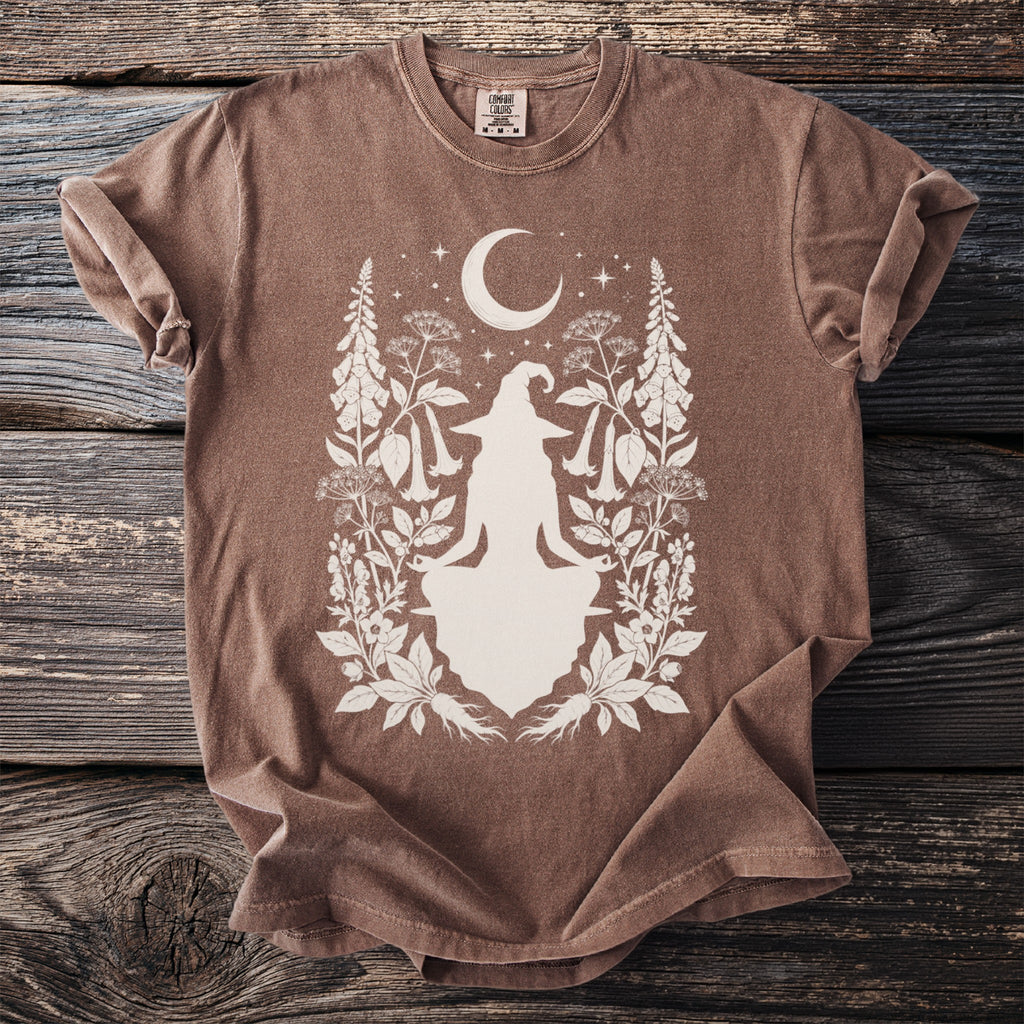 Brown t-shirt with a witch silhouette surrounded by crescent moon, stars, and botanical elements.