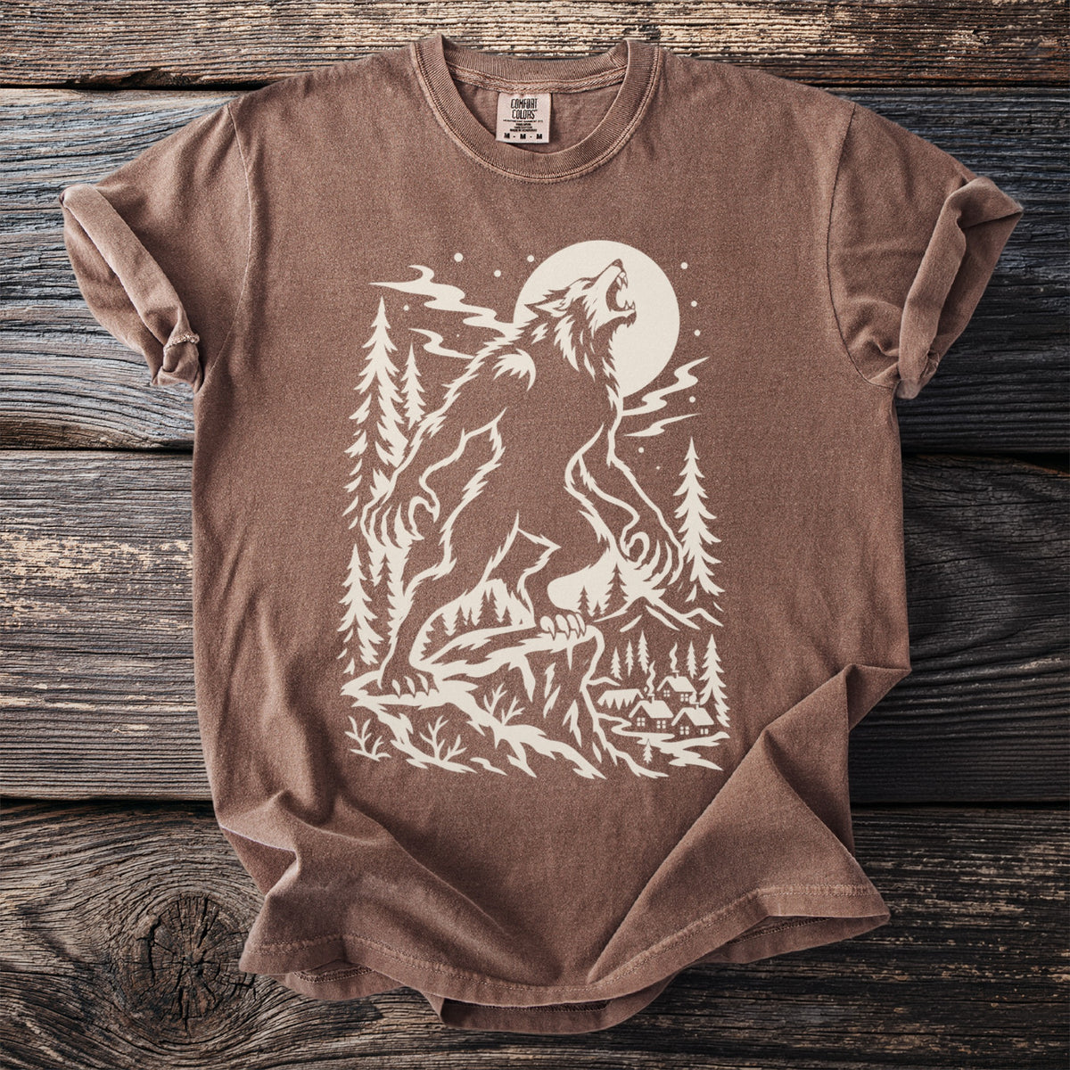 Brown t-shirt with a cream graphic of a werewolf howling at the moon over a village.