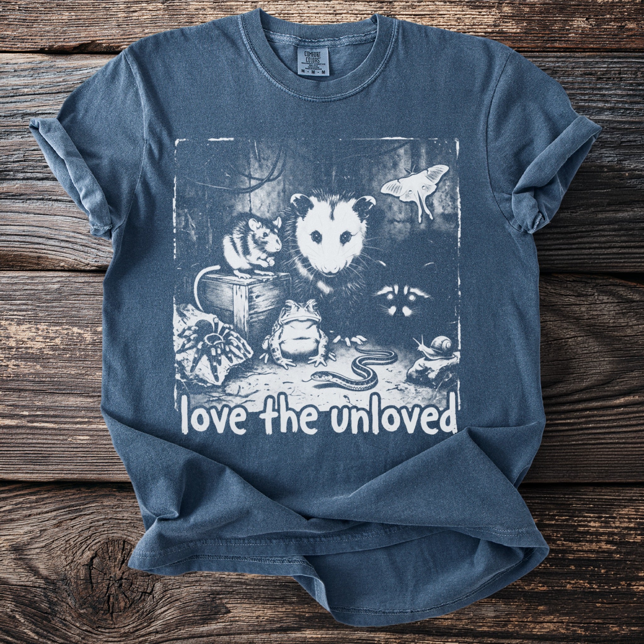 T-shirt with a graphic featuring an opossum, mouse, frog, snake, moth, spider, raccoon, and snail, with text "love the unloved."