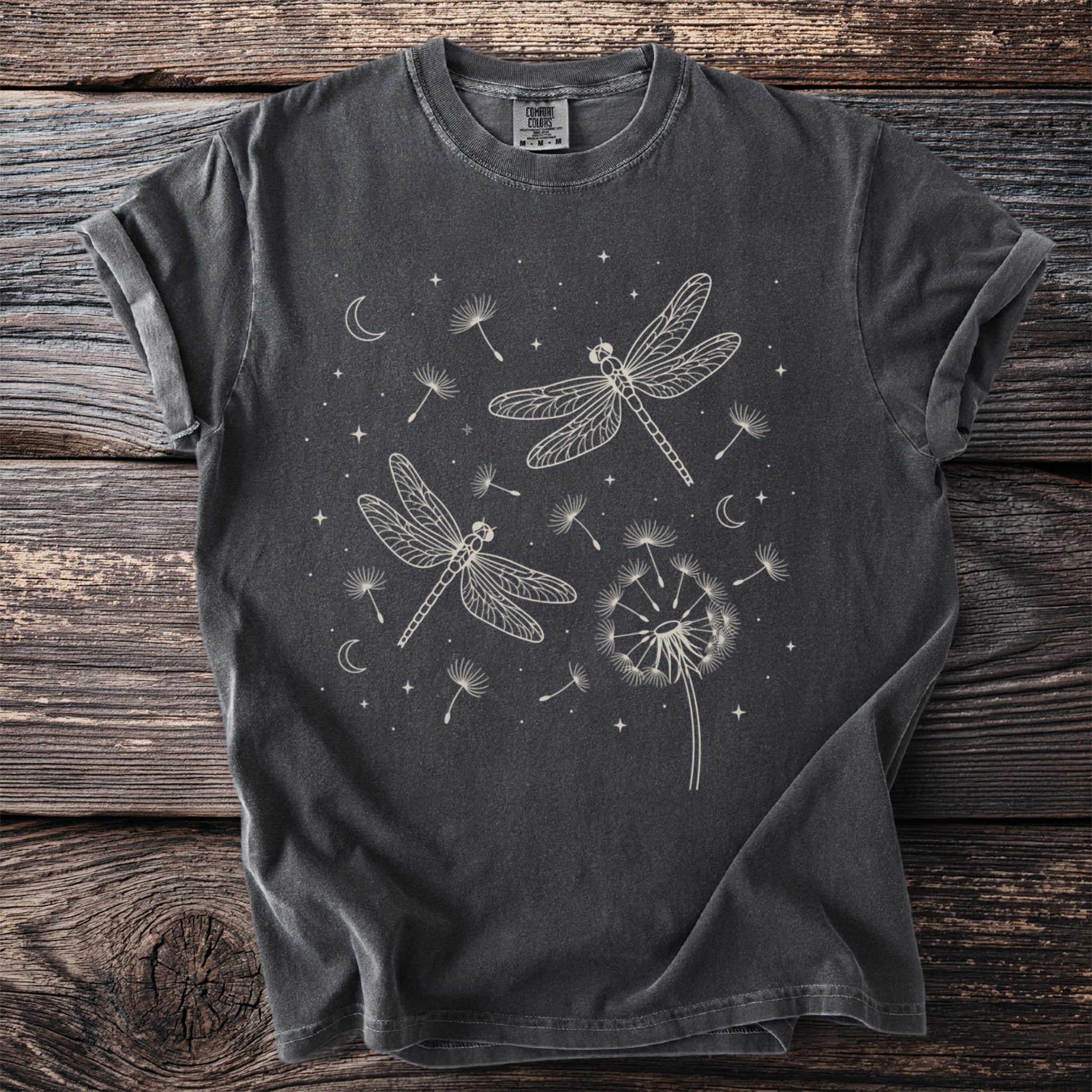 Dark gray t-shirt with cream line art of dragonflies, dandelions, moons, and stars.