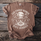 Brown t-shirt with graphic of witches around a campfire and text "GOD FORBID WOMEN HAVE HOBBIES".