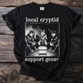 T-shirt with "local cryptid support group" text and image of three anthropomorphic wolves in a meeting.