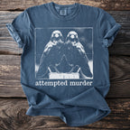 Blue t-shirt with a graphic of two mirrored birds and the text "attempted murder".