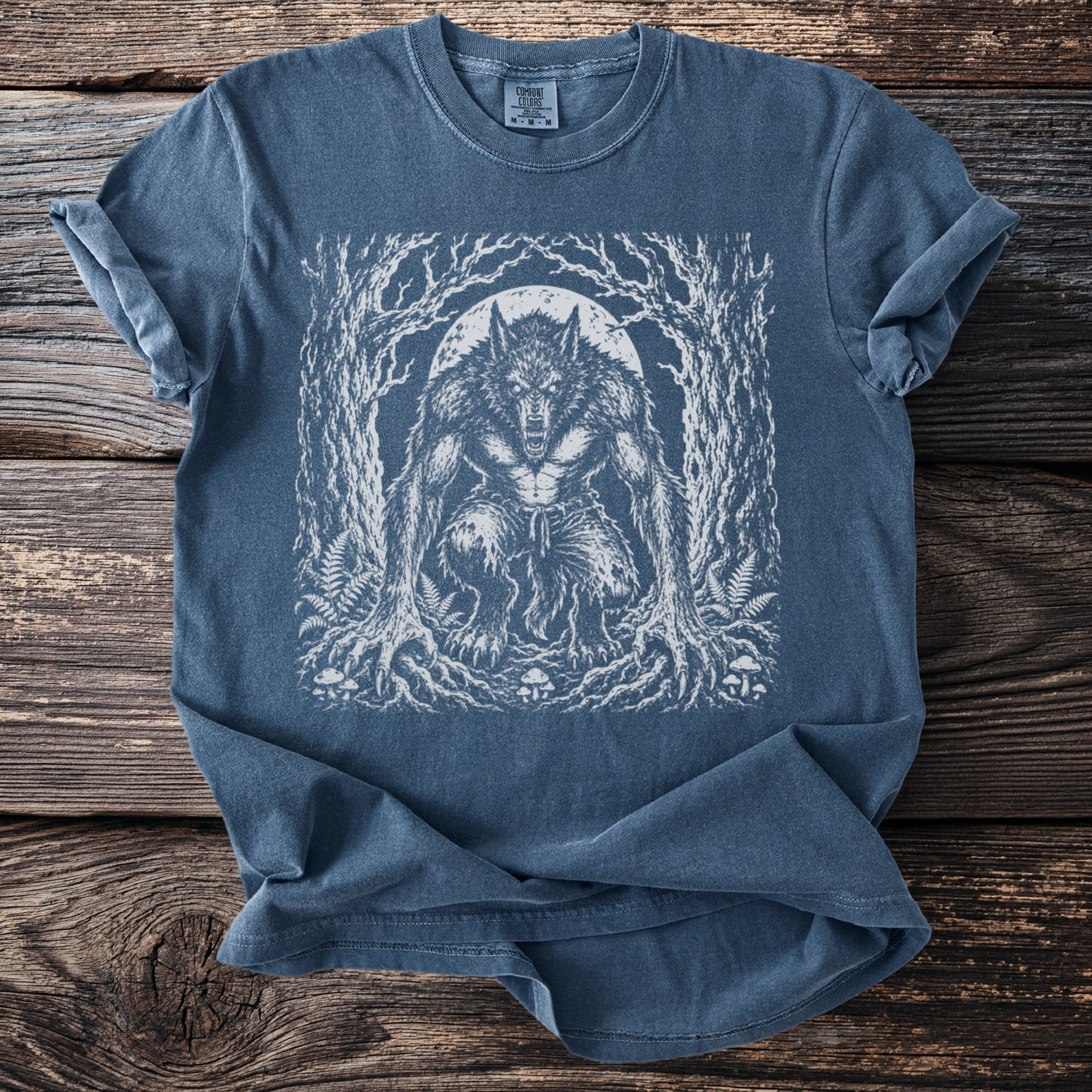 Blue t-shirt with white werewolf graphic in forest scene under a moon.