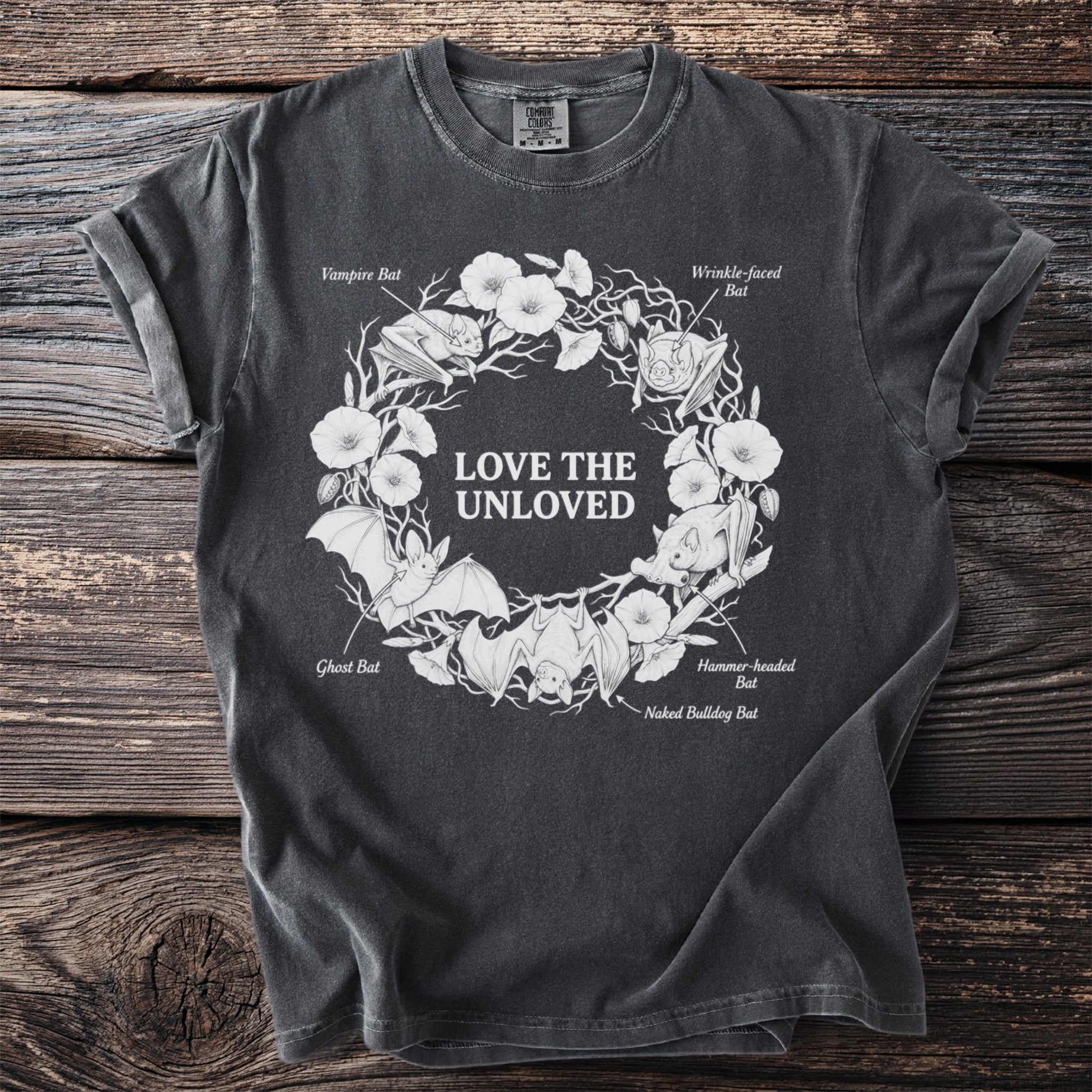 Dark gray t-shirt with a white graphic of bats and flowers, reading "LOVE THE UNLOVED".