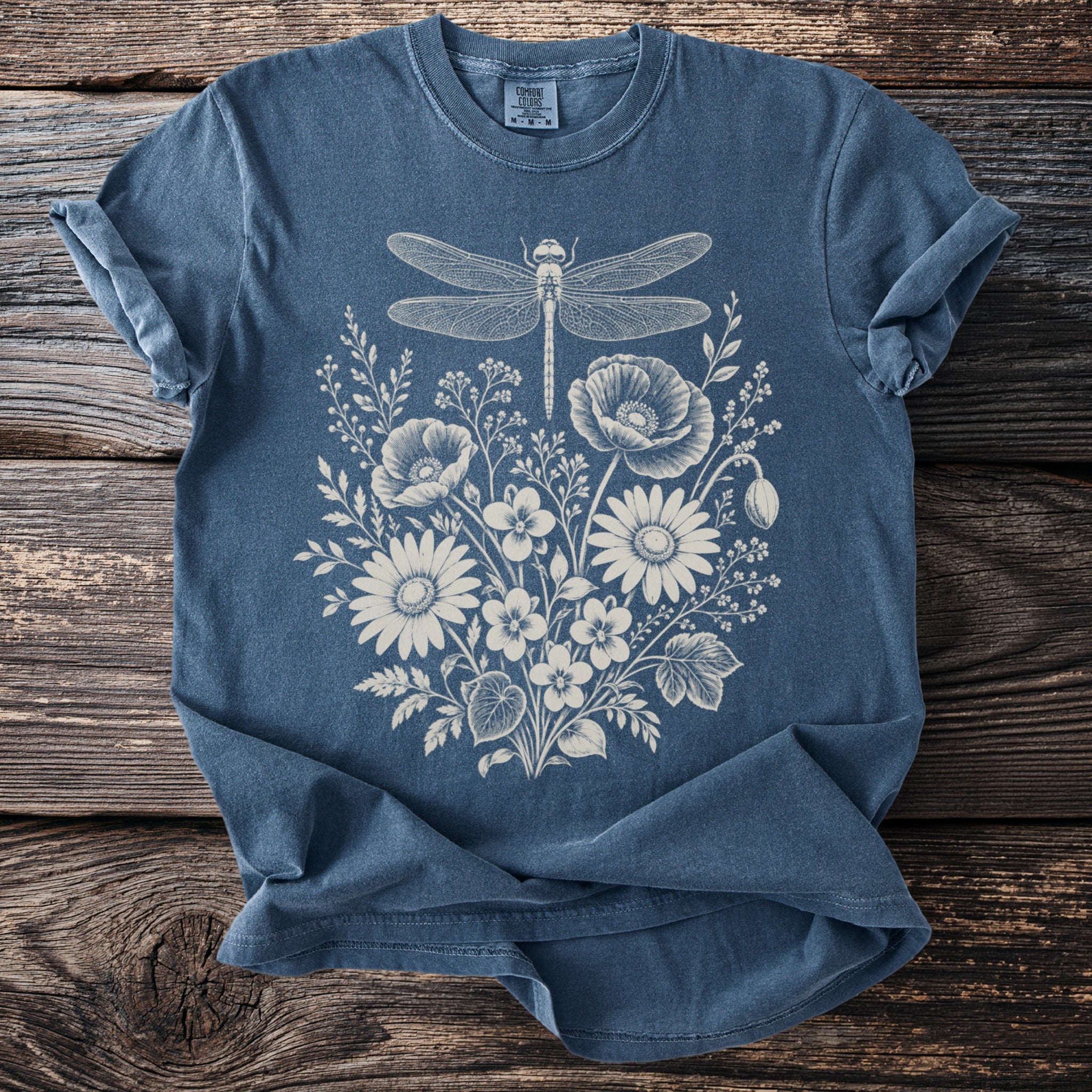 Blue t-shirt with a white line drawing of a dragonfly above a bouquet of flowers.