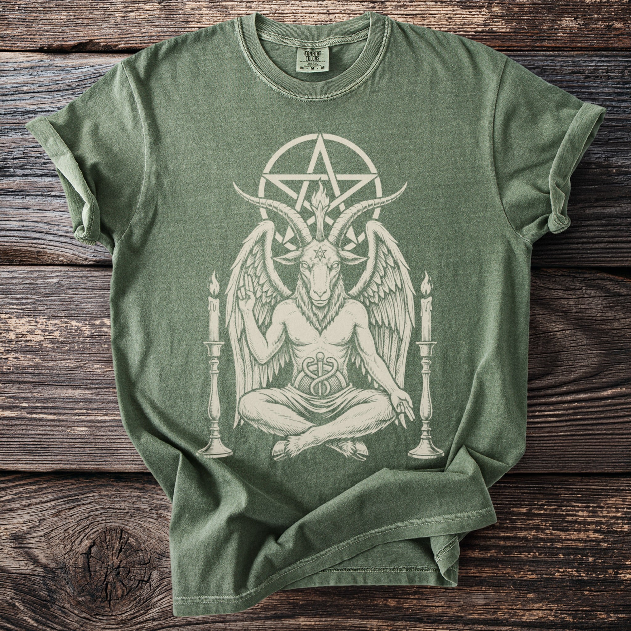 Green t-shirt with Baphomet design, pentagram, and candles, on a wooden background.