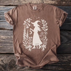 Brown t-shirt with silhouette of witch holding moon and surrounded by botanical illustrations.