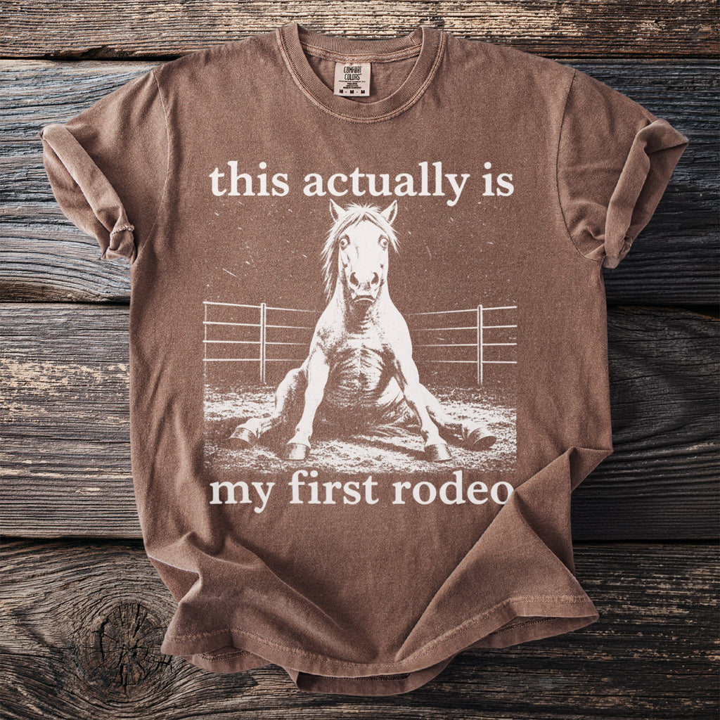 Brown t-shirt with white text and distressed horse graphic: "this actually is my first rodeo"