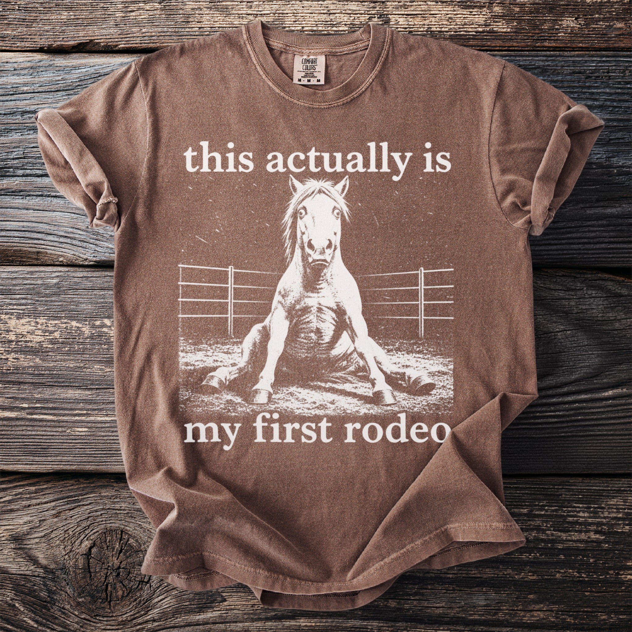 Brown t-shirt with white text and distressed horse graphic: "this actually is my first rodeo"
