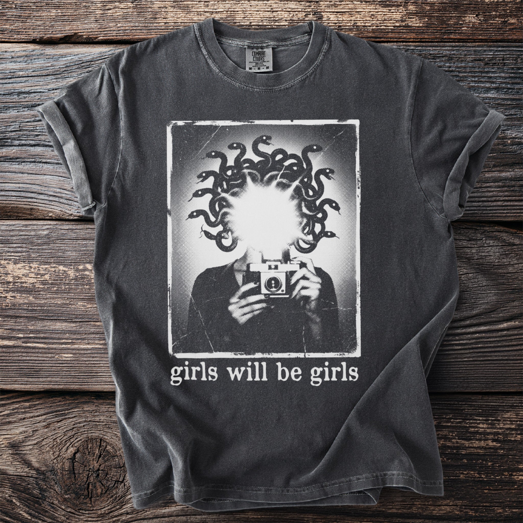 Dark gray t-shirt with graphic of Medusa holding a camera, text "girls will be girls."