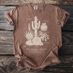Brown t-shirt with a cream botanical illustration of various desert plants and text.
