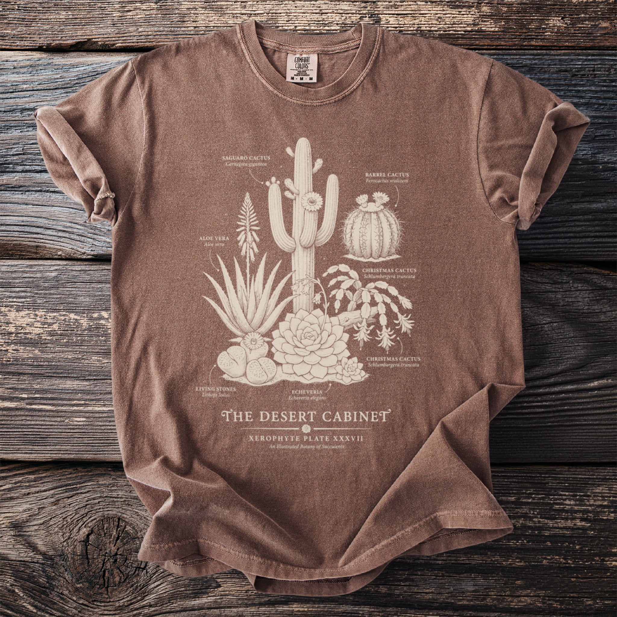 Brown t-shirt with a cream botanical illustration of various desert plants and text.