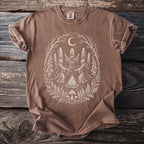 Brown t-shirt with a graphic of robed figures dancing around a campfire under a crescent moon.