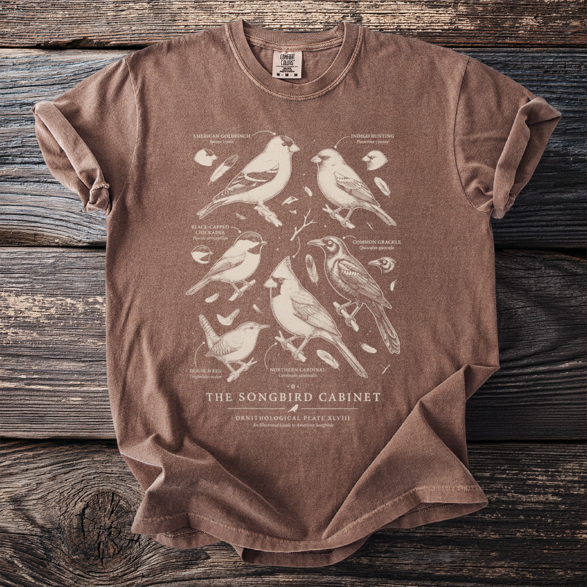 Brown t-shirt with a vintage illustration of six birds and "The Songbird Cabinet" text.