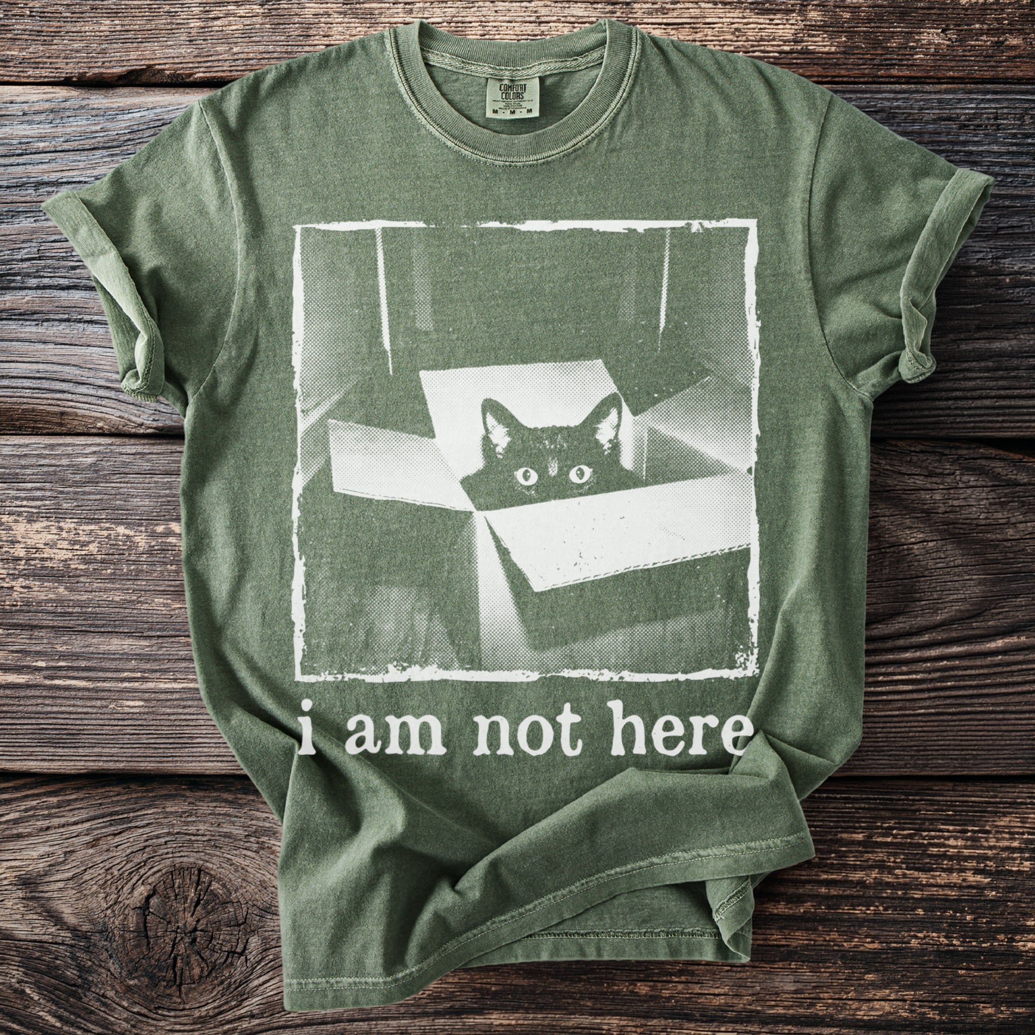 Green t-shirt with a black cat peeking out of a box and text "i am not here".