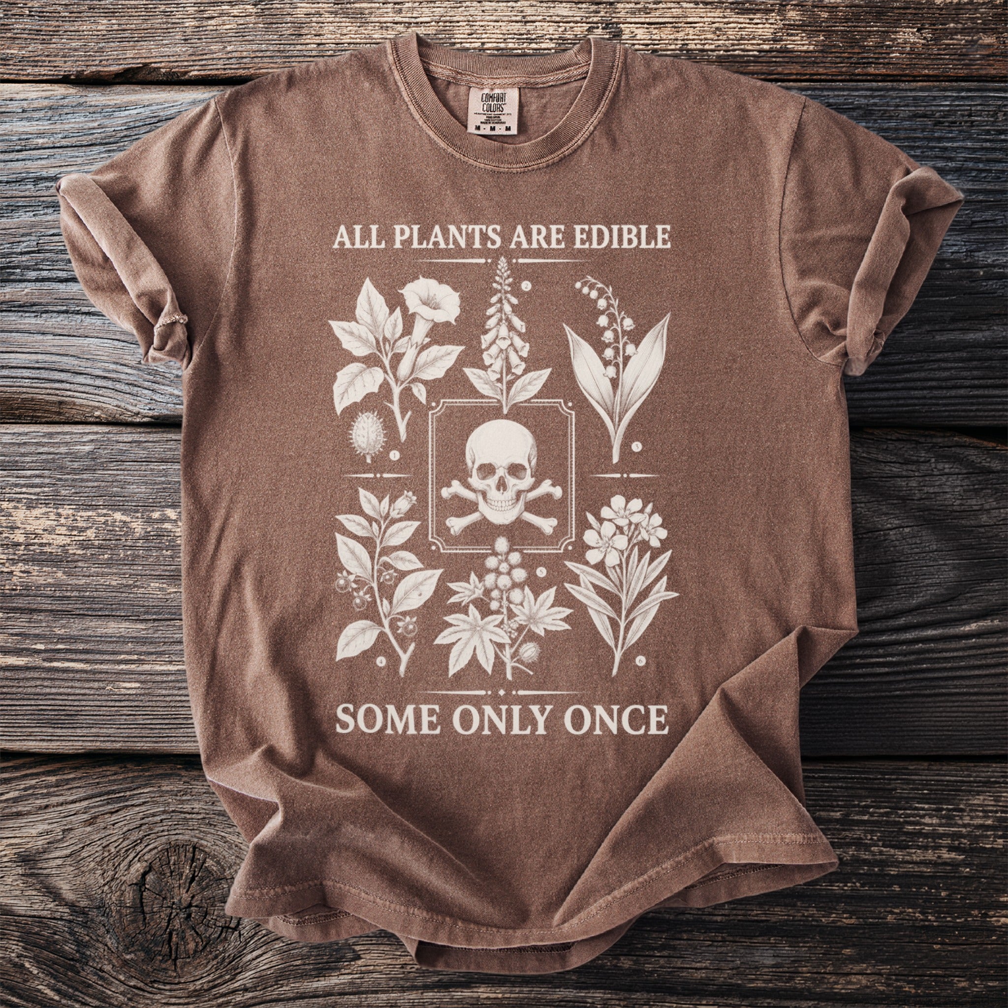 Brown t-shirt with white graphic of skull, crossbones, and plants with text.