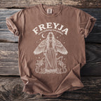Brown t-shirt with a white graphic of Freyja, Norse goddess of love, with wings and cats.