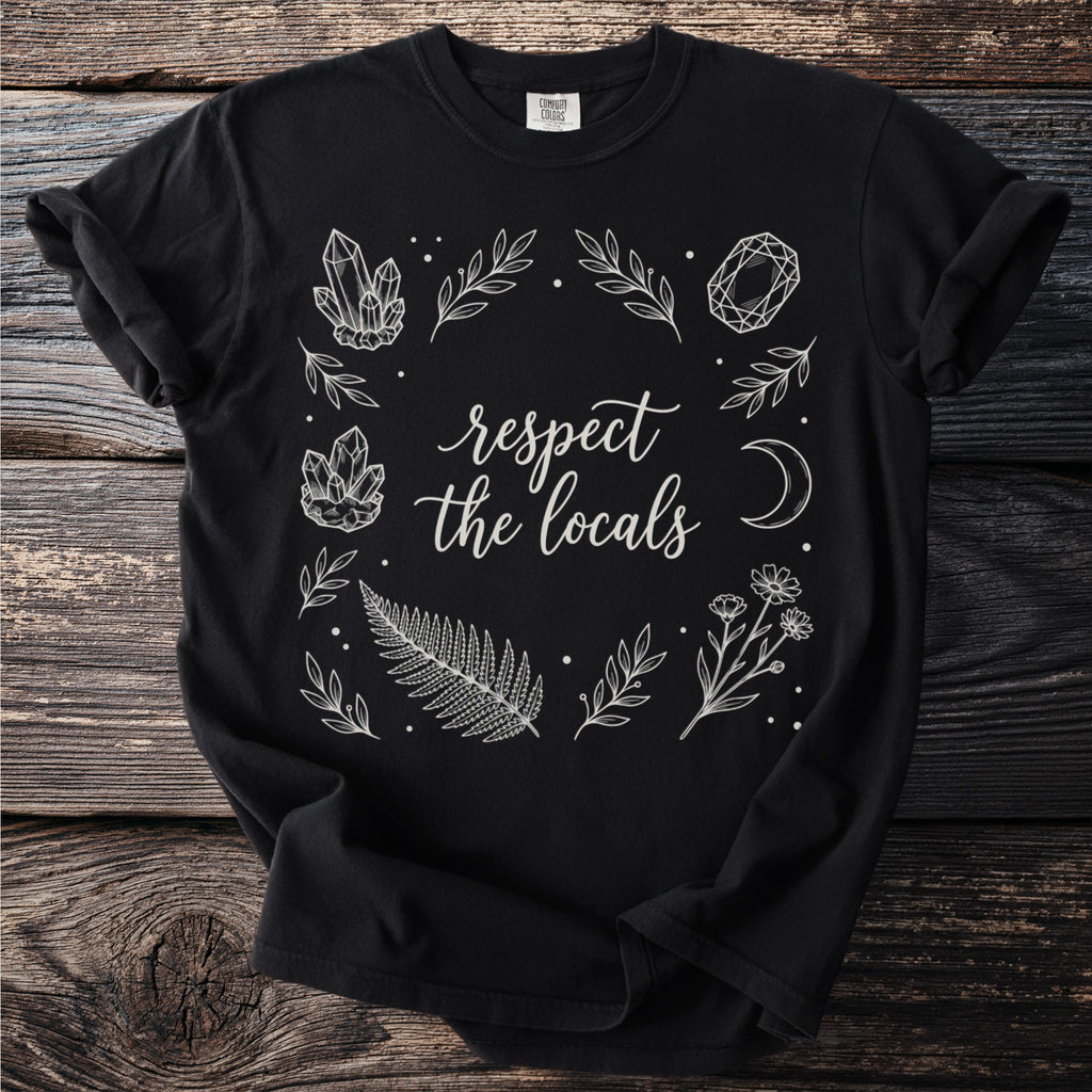 Black t-shirt with white line art of crystals, leaves, fern, flowers, moon, and text.