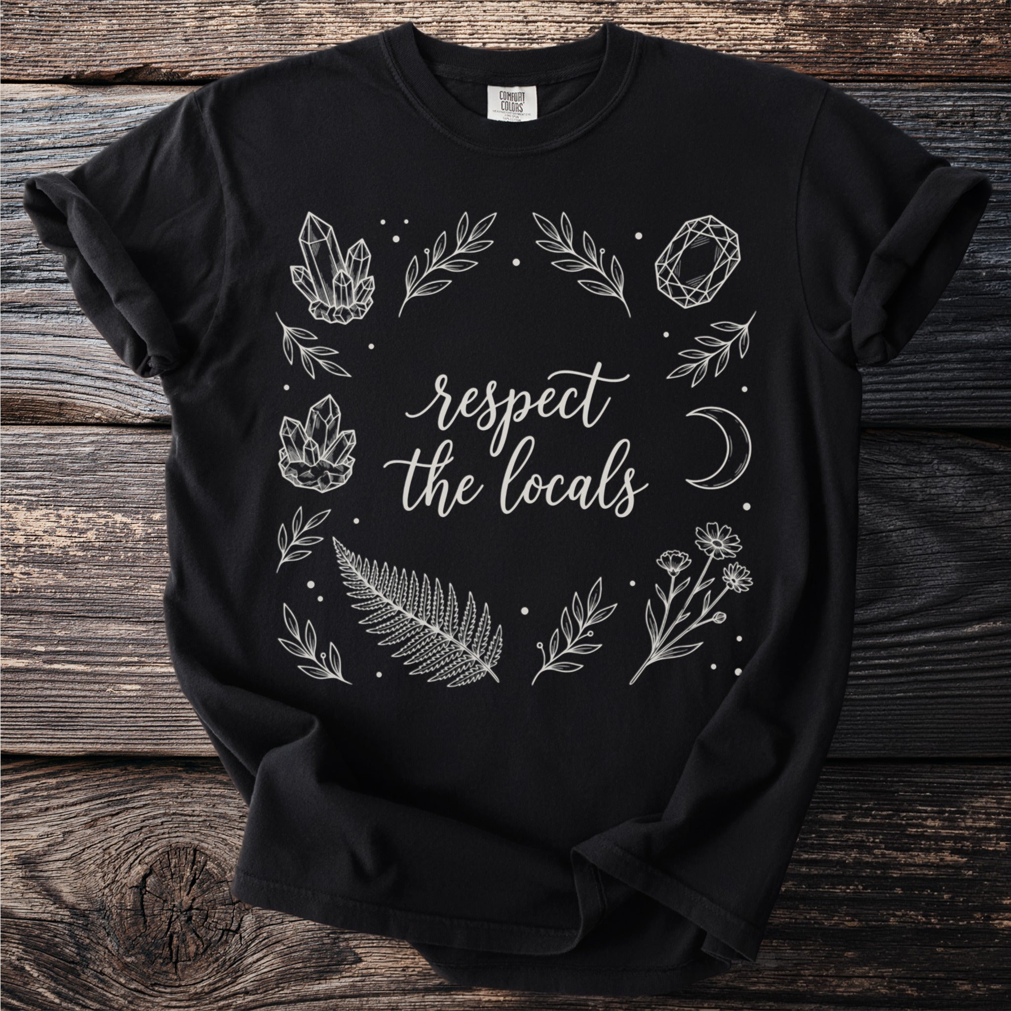 Black t-shirt with white line art of crystals, leaves, fern, flowers, moon, and text.