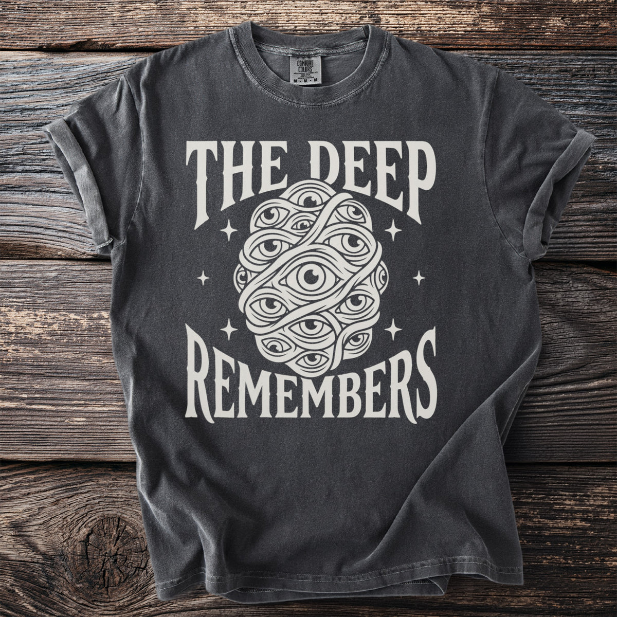 Dark t-shirt with text "THE DEEP REMEMBERS" and an illustration of many eyes.