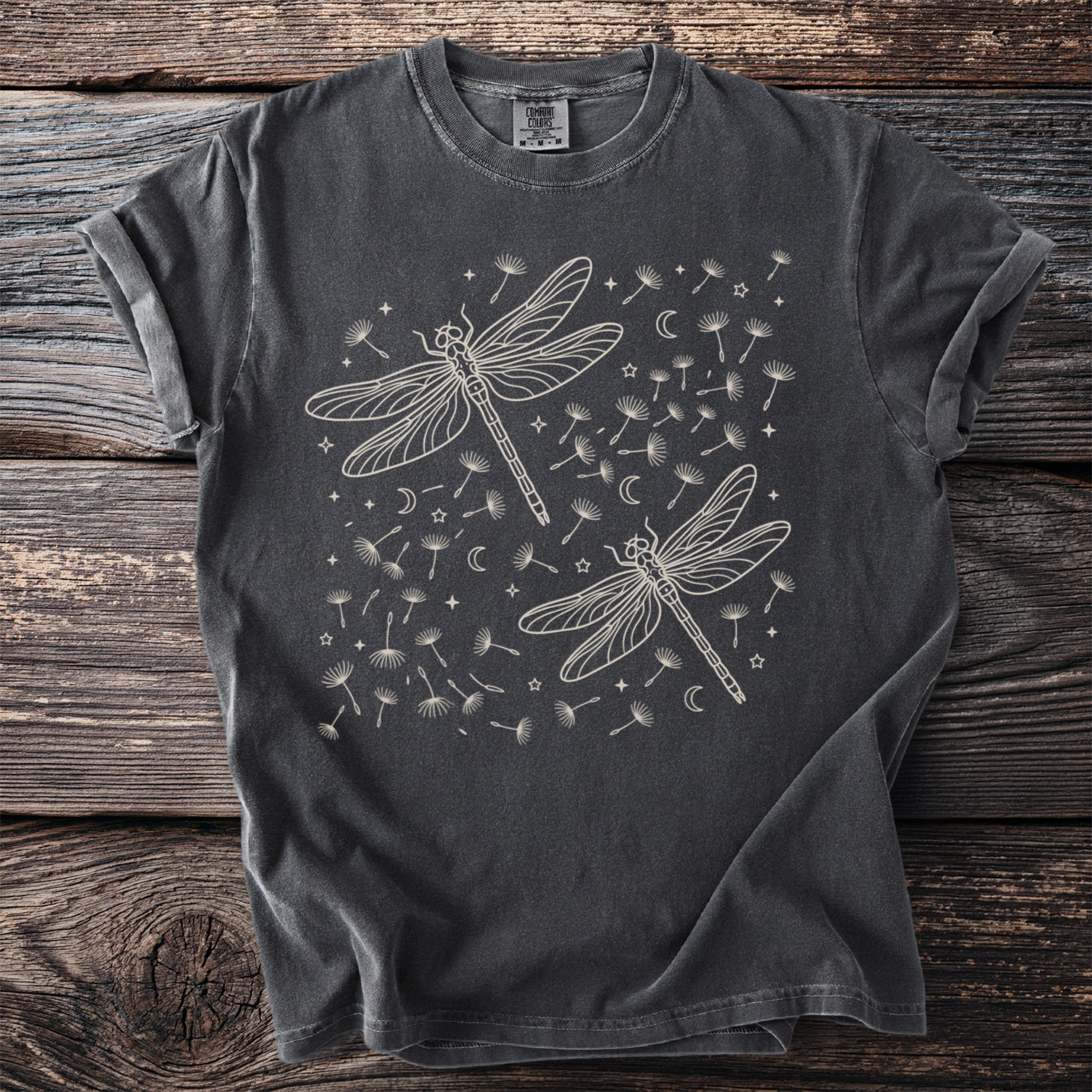 Charcoal t-shirt with two cream line-art dragonflies surrounded by dandelions, moons, and stars.