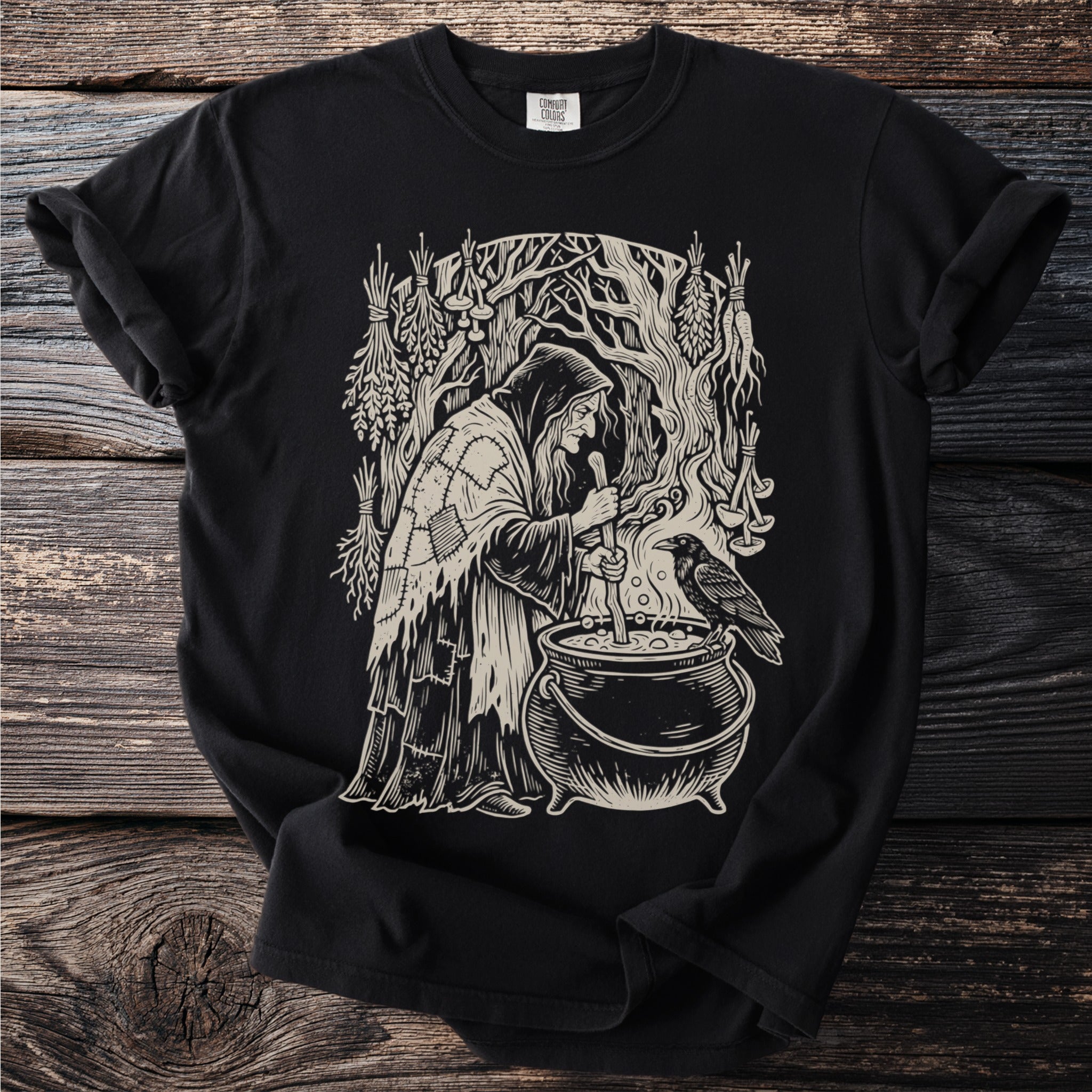 Witch stirring cauldron with raven and herbs, black t-shirt graphic.