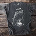 T-shirt with white line art of a crow holding a decorative orb amidst stars.